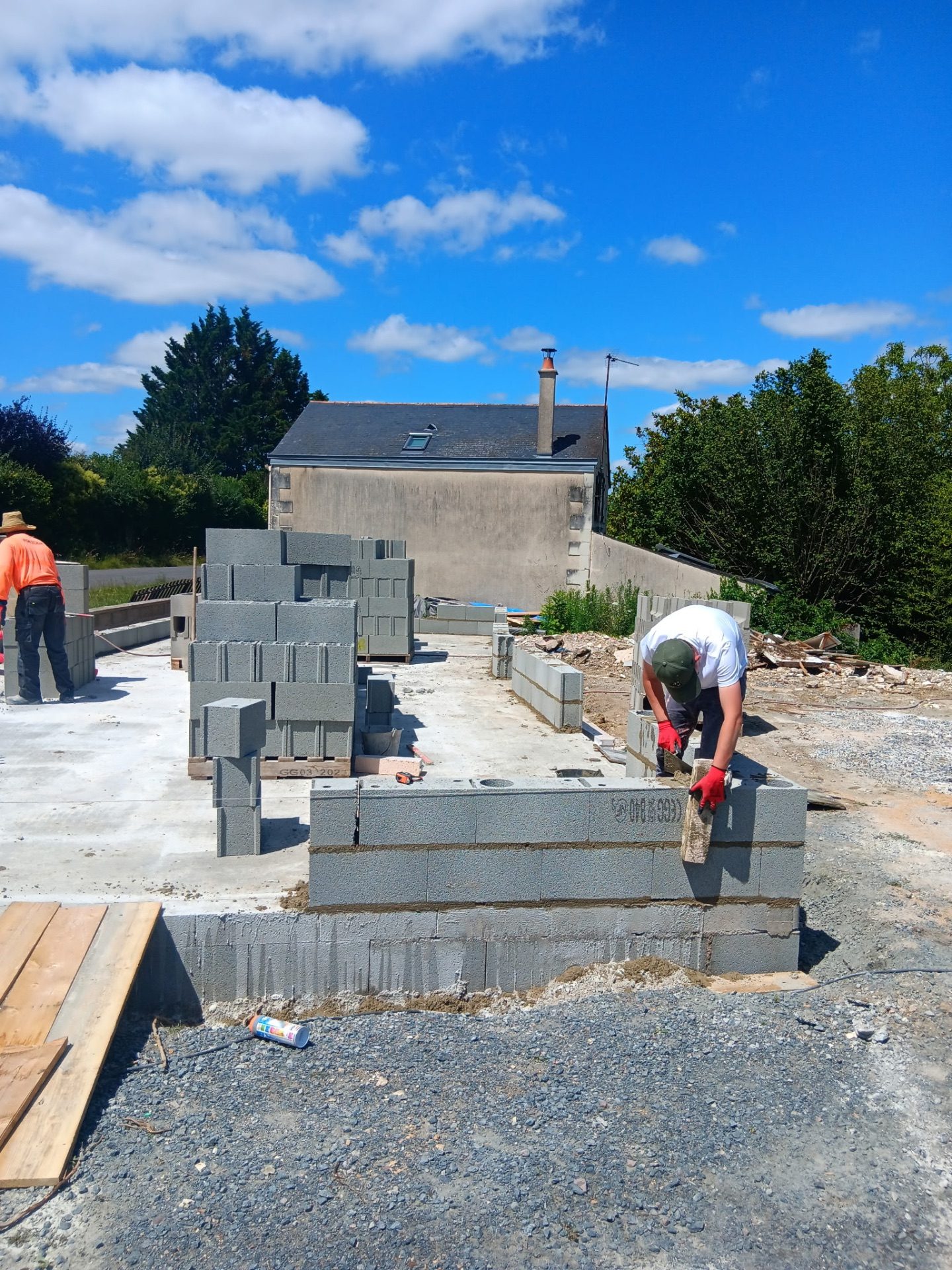 Maçon élevant un mur en parpaings sur dalle béton lors d'une construction près de Saumur
