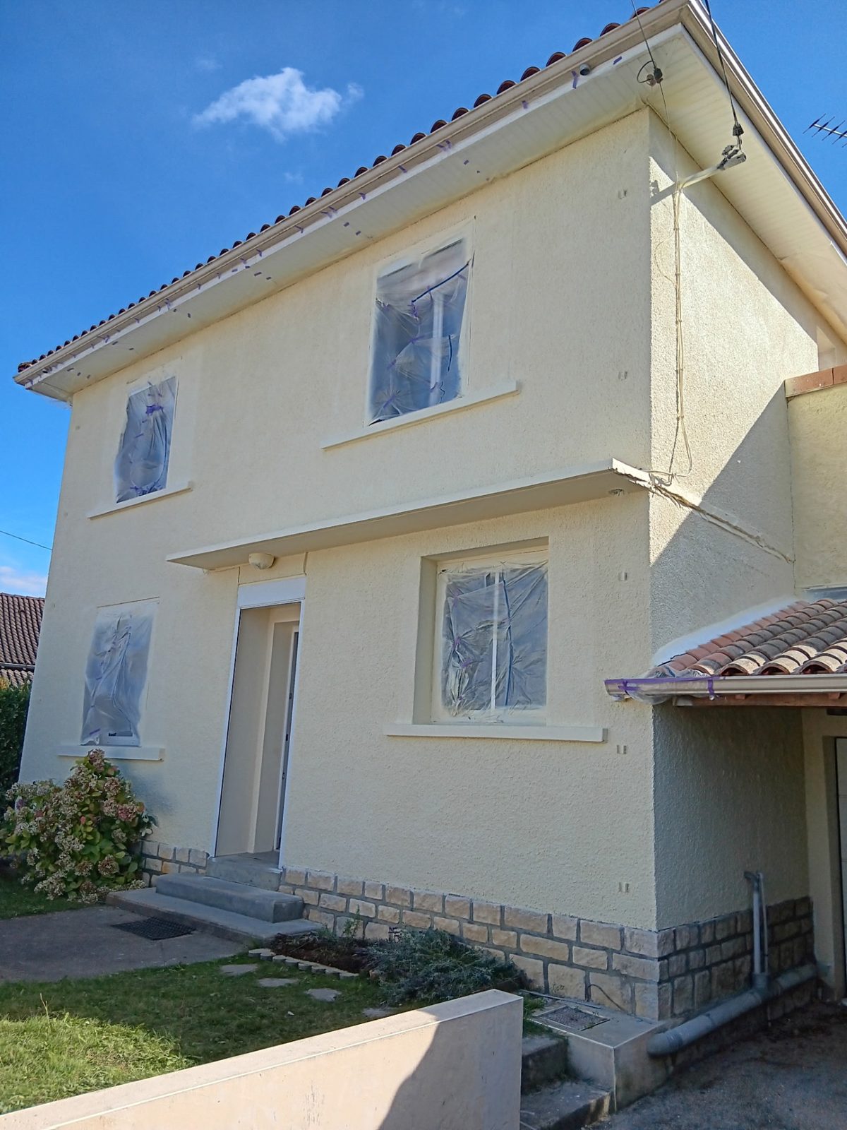 Façade de maison peinte en ton crème avec menuiseries protégées