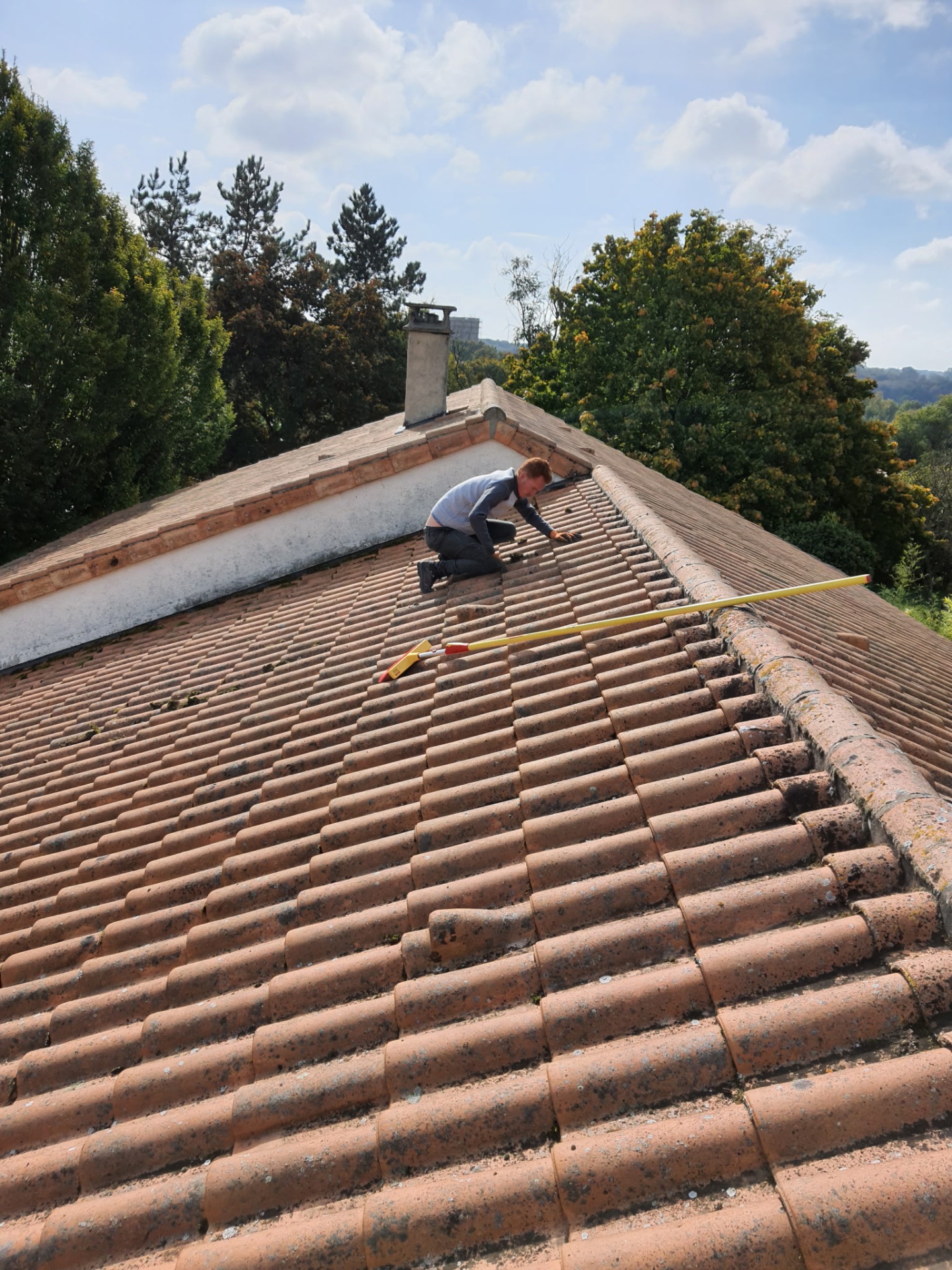 Démoussage manuel d'une toiture en tuiles romanes par un couvreur
